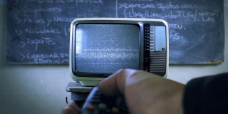 在一所学校的教室里，手持遥控器打开带有测试信号的旧电视。关闭了。