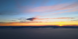 鸟瞰图中，彩色的日落笼罩在白色浓密的雾霭中，远处地平线上群山的黑色剪影
