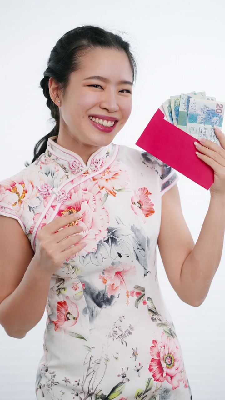 中国/亚洲妇女穿着旗袍，白色花卉图案的衣服，手拿红色的钞票给她的家人，亲戚和朋友，祝新年快乐，富有，幸福，和幸运