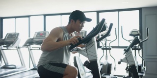 慢动作场景:亚洲青年男子在自行车运动器械上跑步，在健身房锻炼和锻炼有氧运动，以达到运动训练的生活方式理念
