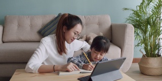 亚洲家庭，女儿在妈妈的帮助下用平板电脑做作业