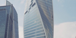 蓝色多云的天空背景下扭曲的摩天大楼的底部视图。行动。玻璃幕墙高层建筑在商业城市中心。