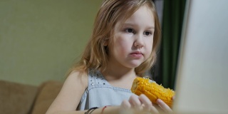 十几岁的女孩吃着煮熟的甜玉米，看着笔记本电脑屏幕