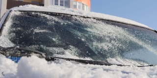 在一个阳光明媚的日子里，手动汽车刷从汽车引擎盖上扫雪