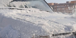 在一个阳光明媚的冬日，用手刷清除车上的积雪