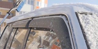 一位妇女的手拿着一把刷子从一辆SUV的车顶扫雪