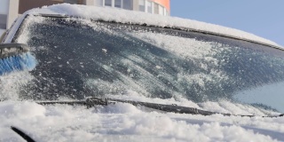 一个女人的手拿着一把刷子，从汽车挡风玻璃上扫雪