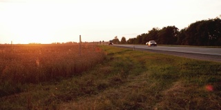 傍晚，在美丽的日落背景下，一列汽车在乡村道路上的移动。汽车和卡车。文本复制空间，延时