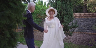 在春夏季公园的户外，一对兴奋的老年夫妇欢快地跳舞。幸福爱着的白种男女穿着婚纱慢动作跳舞，欣喜不已。爱的概念。