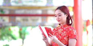 亚洲年轻女子，穿着红色的中国传统旗袍装饰，拿着红色的旗袍信封，上面写着中文的祝福是一个好运气的中国新年快乐