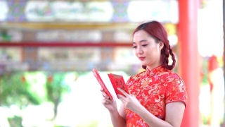 亚洲年轻女子，穿着红色的中国传统旗袍装饰，拿着红色的旗袍信封，上面写着中文的祝福是一个好运气的中国新年快乐视频素材模板下载