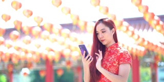 美丽的亚洲妇女穿着传统的中国旗袍服装按电话号码在户外。春节快乐
