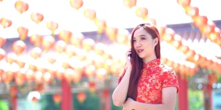 亚洲美女身穿红色中国传统旗袍，用手机装饰中国新年主题。