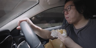 男人一边开车一边吃汉堡。