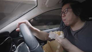男人一边开车一边吃汉堡。视频素材模板下载