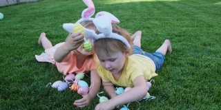 快乐的小妹妹们躺在绿色的草地上玩复活节彩蛋。