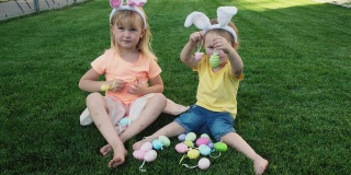 快乐的小妹妹们坐在绿色的草地上玩复活节彩蛋。