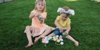 快乐的小妹妹们坐在绿色的草地上玩复活节彩蛋。