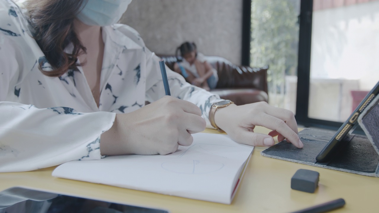 一个戴着医用口罩在笔记本上写字的女人在家工作