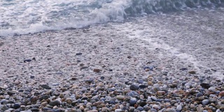 海浪在海边，沙滩上有石头。海浪拍打着卵石滩。鹅卵石和海浪