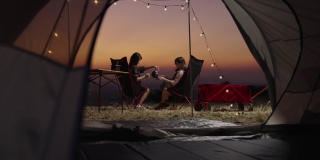 年轻女子休息在旅游帐篷和燃烧篝火看日落与你的朋友在假期。亚洲人，野营，朋友，帐篷，日落，游客。