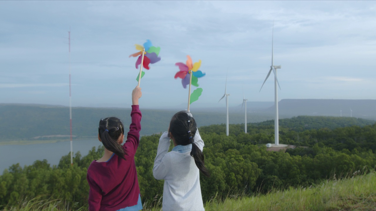 在风力发电场里，亚洲女孩们正在玩风力发电玩具