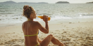 一个穿着泳装的孤独女人在沙滩上喝酒。离别的爱情，和丈夫离婚，糟糕的关系。酒类消费定义概念