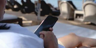 在海上，女人光着脚交叉腿躺在沙滩床上用手机