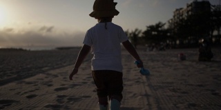 小男孩在夕阳下的沙滩上玩沙子。