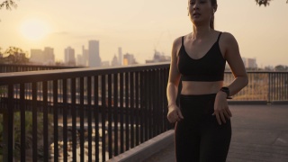 年轻的女运动员跑步休息疲惫后，在城市的夕阳下进行有氧运动锻炼。慢跑的生活方式健康。视频素材模板下载