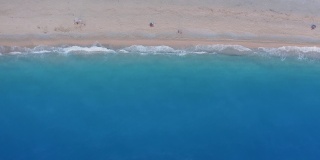 希腊莱夫卡达的米洛斯海滩。从上往下看，金色的沙滩和荧光的绿松石色的海浪。在日落时分欣赏夏日美景的人们