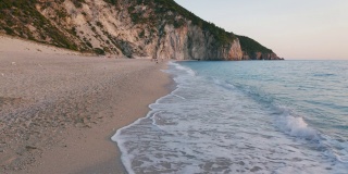 希腊爱奥尼亚岛莱夫卡达美丽的米洛斯海滩的低空鸟瞰图。夕阳金色的阳光和原始的海浪打破了蓝绿色的大海在岸边