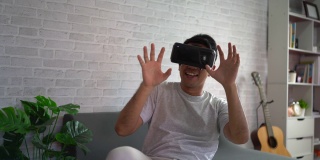 亚洲男人在家玩虚拟现实游戏娱乐，亚洲男人在假期在家快乐。快乐女人玩超时空VR技术概念。