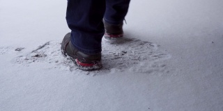 雪地上穿着黑色靴子的男人的腿。他跳舞取暖，然后走出镜头，留下脚印。