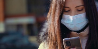 近距离观察，一名妇女戴着医用口罩，在城市街道上用手机发送信息，以防止空气污染和冠状病毒感染