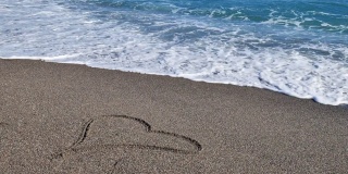 心形符号绘制在沙滩上，背景是柔和的蓝色波浪。海浪的泡沫洗去了画在沙滩上的一颗心。情人节，浪漫的概念。