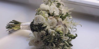 婚礼金戒指躺在美丽的婚礼白玫瑰花束在白色的窗台上