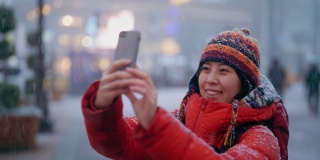 冬天，年轻的女游客在城市的雪地里用智能手机享受观光和自拍