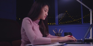 亚洲女性使用笔记本电脑工作到很晚，晚上在家加班