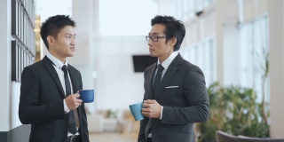 2名亚洲华裔白领西装革面，在办公室走廊喝酒休息