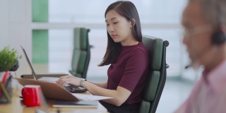 亚裔中国美女在办公室用笔记本电脑在同事旁边打字