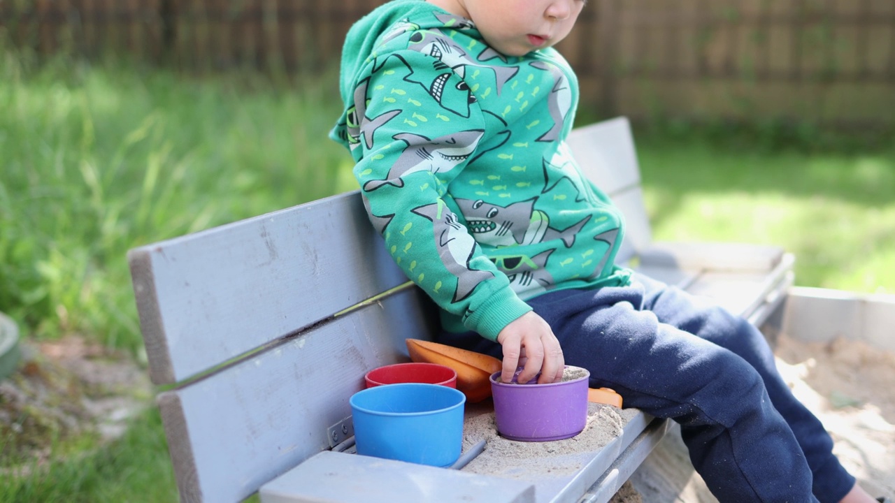 白种人小孩男孩在阳光明媚的日子里在院子外面玩沙盒沙塑料模具