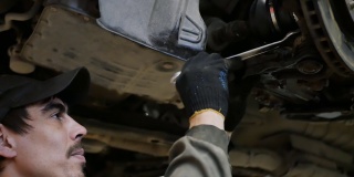 汽车下面的一个男性汽车修理工用扳手拧紧了螺母