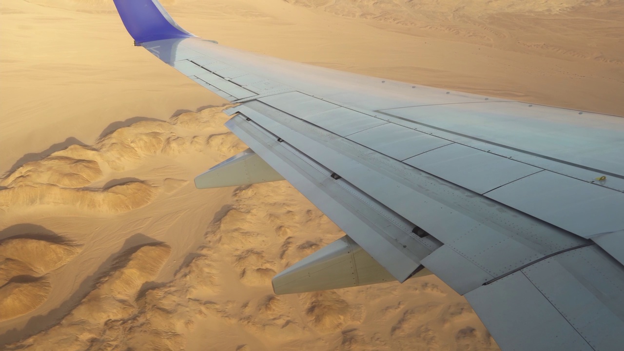 飞机飞越高山和沙漠，窗外的景色就在飞机的机翼和襟翼上。