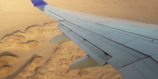 飞机飞越高山和沙漠，窗外的景色就在飞机的机翼和襟翼上。