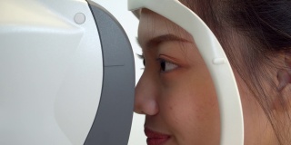 特写:亚洲年轻女子在眼科医生的办公室用专业设备检查她的视力