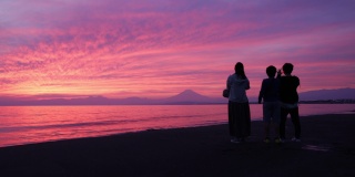 女性朋友和儿子在日落时分的海滩上拍照