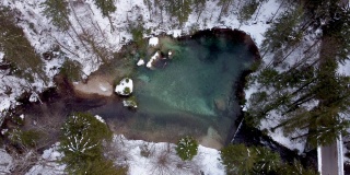 空中画图:冬日里，清新的泉水在白雪皑皑的松树林中流淌。4 k UHD。