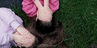 两个漂亮的千禧一代朋友躺在公园或草坪上的绿草地上。白人女孩笑着一起玩。俯视图的镜头