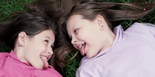 两个漂亮的千禧一代朋友躺在公园或草坪上的绿草地上。白人女孩笑着一起玩。俯视图的镜头